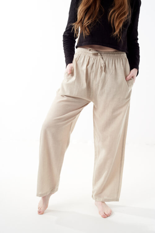 Osoba stoi na białym tle w czarnej koszulce i luźnych beżowych spodniach