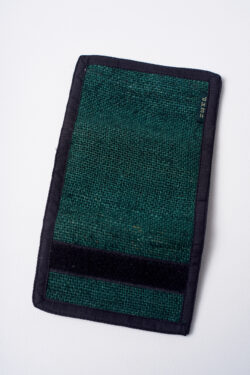 Tył zielonego portfela konopnego, częściowo rozłożony, z widocznym czarnym rzepem na krawędzi, na białym tle