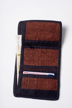 Wnętrze brązowego portfela konopnego z czarnymi elementami wykończenia, trzema mniejszymi kieszeniami, w tym jedną na zamek, oraz jedną dużą kieszenią, w której znajduje się banknot, z mniejszej kieszeni wystaje dokument tożsamości na białym tle