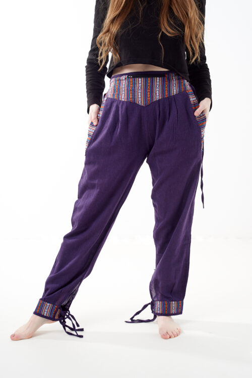 Osoba w czarnej koszulce stoi na białym tle w fioletowych spodniach z wstawkami z materiału gheri