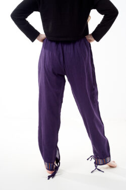 Osoba w czarnej koszulce stoi tyłem na białym tle w fioletowych spodniach z wstawkami z materiału gheri