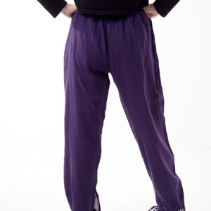 Osoba w czarnej koszulce stoi tyłem na białym tle w fioletowych spodniach z wstawkami z materiału gheri