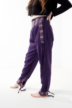 Osoba w czarnej koszulce stoi na białym tle w fioletowych spodniach z wstawkami z materiału gheri