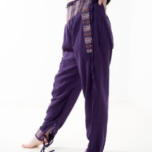 Osoba w czarnej koszulce stoi na białym tle w fioletowych spodniach z wstawkami z materiału gheri