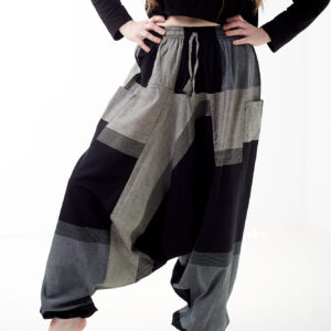 Osoba na białym tle w czarnej koszulce i luźnych czarno szarych patchworkowych szarawarach