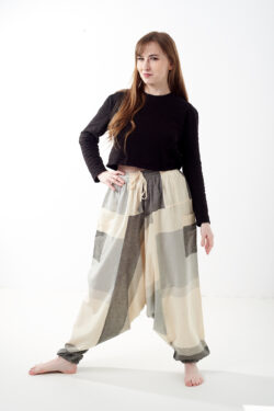 Osoba na białym tle w czarnej koszulce i luźnych beżowo szarych patchworkowych szarawarach z kieszeniami