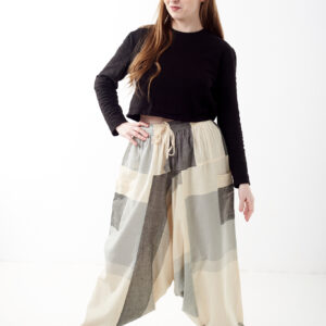 Osoba na białym tle w czarnej koszulce i luźnych beżowo szarych patchworkowych szarawarach z kieszeniami