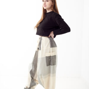 Osoba na białym tle w czarnej koszulce i luźnych beżowo szarych patchworkowych szarawarach z kieszeniami