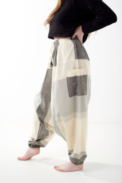 Osoba na białym tle w luźnych beżowo szarych patchworkowych szarawarach z kieszeniami