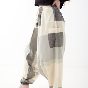 Osoba na białym tle w luźnych beżowo szarych patchworkowych szarawarach z kieszeniami