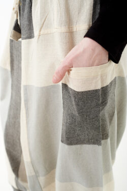 Osoba na białym tle wkłada rękę do kieszeni luźnych beżowo szarych patchworkowych szarawarów