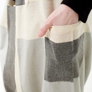 Osoba na białym tle wkłada rękę do kieszeni luźnych beżowo szarych patchworkowych szarawarów