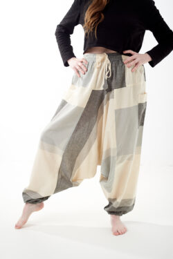 Osoba na białym tle w luźnych beżowo szarych patchworkowych szarawarach z kieszeniami