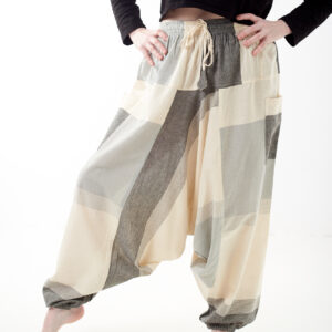 Osoba na białym tle w luźnych beżowo szarych patchworkowych szarawarach z kieszeniami