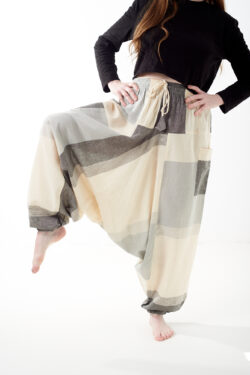 Osoba na białym tle w luźnych beżowo szarych patchworkowych szarawarach z kieszeniami