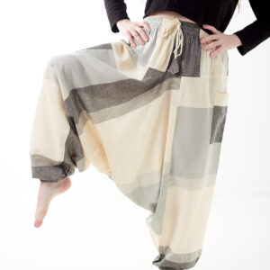 Osoba na białym tle w luźnych beżowo szarych patchworkowych szarawarach z kieszeniami