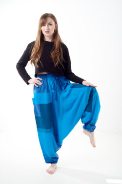 Osoba stoi na białym tle w luźnych niebieskich patchworkowych szarawarach z kieszeniami