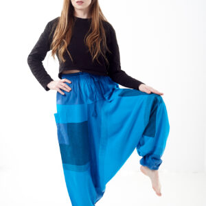 Osoba stoi na białym tle w luźnych niebieskich patchworkowych szarawarach z kieszeniami