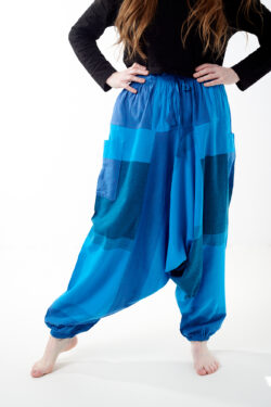 Osoba stoi na białym tle w luźnych niebieskich patchworkowych szarawarach z kieszeniami