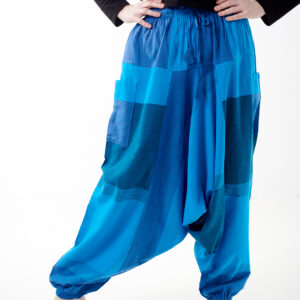 Osoba stoi na białym tle w luźnych niebieskich patchworkowych szarawarach z kieszeniami