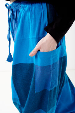 Osoba na białym tle wkłada rękę do kieszeni luźnych niebieskich patchworkowych szarawarów