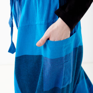 Osoba na białym tle wkłada rękę do kieszeni luźnych niebieskich patchworkowych szarawarów