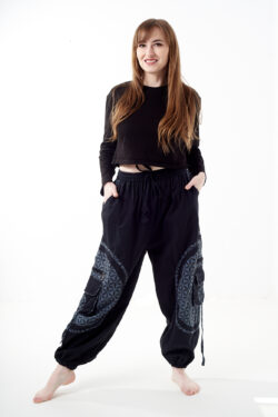 Kobieta stoi na białym tle w czarno-szarych luźnych spodniach cargo z kwiatowym wzorem