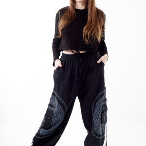 Kobieta stoi na białym tle w czarno-szarych luźnych spodniach cargo z kwiatowym wzorem