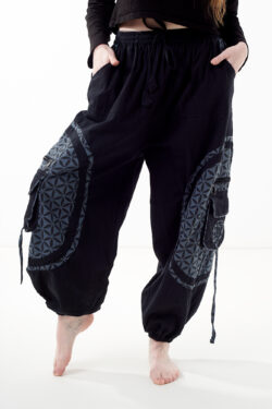 Osoba stoi na białym tle w czarno-szarych luźnych spodniach cargo z kwiatowym wzorem.