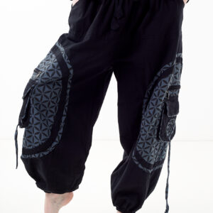 Osoba stoi na białym tle w czarno-szarych luźnych spodniach cargo z kwiatowym wzorem.