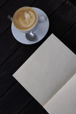 Otwarty notes z ręcznie czerpanym papierem, kawa i drewniany stolik